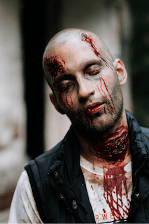 A man dressed up as a zombie with blood dripping from his eyes and neck